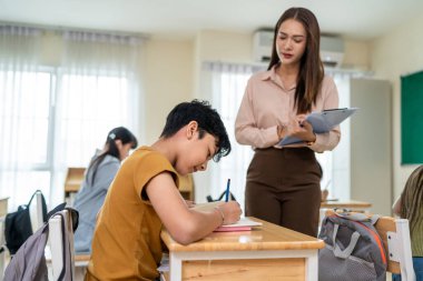 İlkokuldaki sınıfta Asyalı bir öğrenci öğretmeniyle birlikte öğreniyor. Sevimli genç okul çocukları masada oturuyor, ders verirken, ders verirken, ders verirken, kitap yazıyorlar.