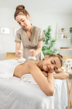 Güzel bir kadın bitkisel poşetlerle Tayland masajı yaptırıyor. Çekici genç kız masaj yatağında uzanıp masaj salonundaki masözden rahatlatıcı fizyoterapi hizmeti alıyor..