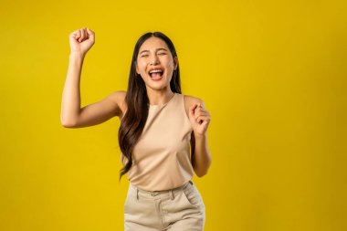 İzole edilmiş sarı arka planda duran Asyalı güzel bir kadının portresi. Çekici genç bayan model, stüdyo çekimlerinde poz verirken ve dans ederken kendine güvenerek gülümserken mutlu ve neşeli hissediyor.