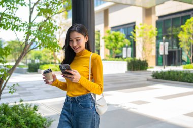Asyalı genç bir kadın şehirde dikilirken akıllı telefon kullanıyor. Çekici, güzel bir kız bir fincan sıcak kahve içiyor, iletişim kuruyor ve şehir içi güvenle cep telefonuyla konuşuyor..