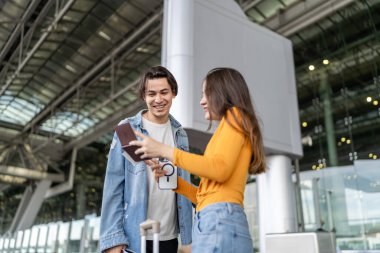 Havaalanı terminalinin dışında bekleyen Asyalı genç çift. Çekici erkek ve kadın arkadaşlar tatil gezisi için uçakla yurtdışına gittikleri için mutlu ve heyecanlı hissediyorlar..