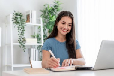 Asyalı çekici kadın evden öğrenirken kitap hakkında notlar alıyor. Masada oturan genç ve güzel bir kız öğrenci, dizüstü bilgisayar kullanıyor, çalışıyor ve ev ödevlerini yapıyor..