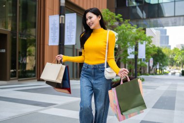 Asyalı genç ve güzel bir kadın mağazada alışveriş yapıyor. Alışveriş torbaları tutan çekici bir kadın. Mutlulukla tek başına yürüyor. Alışveriş merkezinden alışveriş yapmanın keyfini çıkarıyor..