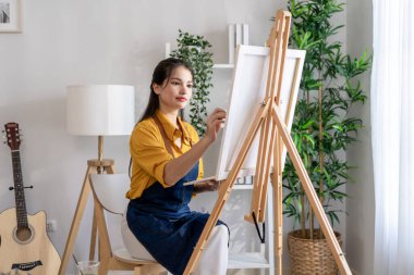 Asian young talented woman artist coloring on painting board in house. Attractive beautiful female draw art picture, creating artwork with watercolor paint and brush enjoy creativity activity at home.