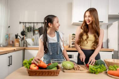Asyalı güzel anne mutfakta küçük kızıyla yemek pişiriyor. Mutlu Aile, çekici ebeveyn anne sağlıklı yiyecekler hazırlamaktan ve küçük kıza evde kahvaltı hazırlamayı öğretmekten zevk alır..
