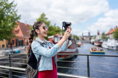 Asyalı kadın gezgin şehirde seyahat ederken kamera kaydı vlog 'u kullanır. Çekici bayan turist sokakta yürürken mutlu ve rahat hissediyor, Danimarka 'da tatil yaparken fotoğraf çekmenin keyfini çıkarıyor..