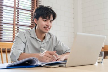 Evde çalışan dizüstü bilgisayar kullanan Asyalı çekici bir adam. Genç erkek öğrenci evdeki oturma odasında teknolojiyle çevrimiçi iletişim kurmak için bilgisayarda sohbet ediyor ve daktilo kullanıyor..