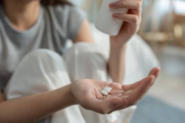 Yatakta uyandıktan sonra ilaç alan hasta kadının ellerini kapat. Çekici genç kız üzgün ve baş ağrısı çekiyor ve evde yatak odasında zihinsel ilaç ve temiz su tutuyor..