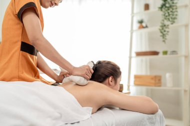 Güzel bir kadın bitkisel poşetlerle Tayland masajı yaptırıyor. Çekici genç kız masaj yatağında uzanıp masaj salonundaki masözden rahatlatıcı fizyoterapi hizmeti alıyor..