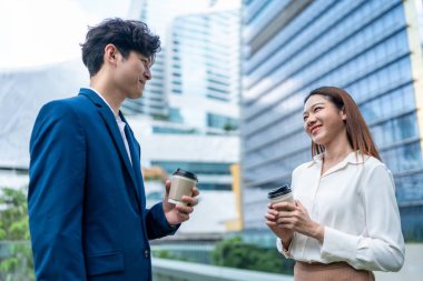 Asyalı işadamı ve kadın şehirde birbirleriyle konuşuyorlar. Çekici çalışan partner insanlar mutlu ve rahatlar, ellerinde bir fincan kahve, boş vakitlerini ofis dışında durarak geçirirler..