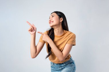 Gri arka planda duran Asyalı güzel bir kadının portresi. Genç, çekici, heyecanlı, mutlu ve neşeli bir kadın model. Stüdyo işyeri çekimine işaret ederken gülümsüyor..