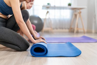 Evdeki oturma odasında egzersiz paspası tutan iki sporcunun fotoğrafını çek. Spor giyim antrenmanında çekici genç kızlar birlikte sağlık yaşam tarzları için yoga germe vücut ile meditasyon yapıyorlar..