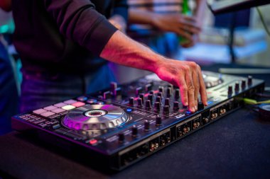 Genç sanatçı DJ 'in müzik mikseri karıştırma ve tırmalama kontrolörünü kapatın. Çekici erkek müzisyen DJ konsol tuşlarına basarak ve neon partisinde elektronik müzik çalarak müziği karıştırırken eğleniyor.