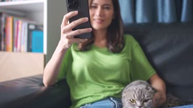 Kadın sandalyede otururken selfie çekiyor.