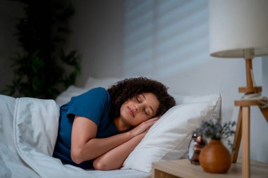 Çekici Latin kadın geceleri karanlık bir yatak odasında yatıyordu. Genç bayan kendini mutlu ve rahat hissediyor, rahat bir yastık ve battaniyeyle dinleniyor, evinde huzurlu bir hafta sonunun keyfini çıkarıyor..