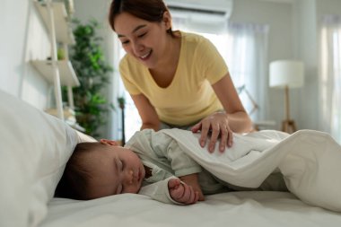 Asyalı anne, evdeki yatak odasında uyuyan bebeğine bakıyor. Çekici ebeveyn, küçük bebeğe bakar. Rahat bir şekilde uzanır ve dinlenir. Erken çocukluk gelişimi için uyur..