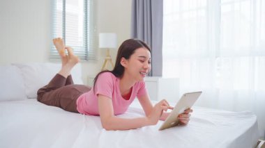 Tablet kullanarak yatağa uzanan genç bir kadın.