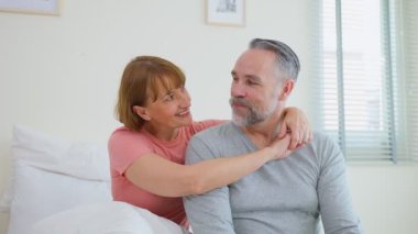 Yatak odasında birlikte oturan çift gülümsüyor.