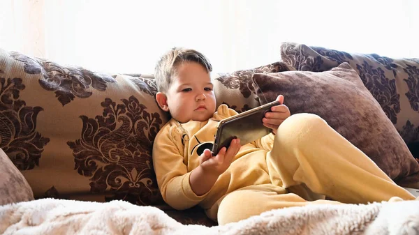 Uma Criança Pijama Olha Para Telefone Sofá Foto Alta Qualidade — Fotografia de Stock