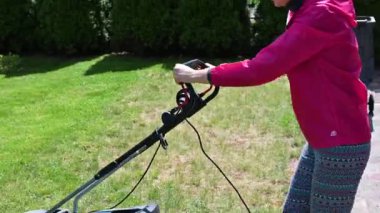 Genç kız elektrikli çim biçme makinesiyle çim biçiyor.