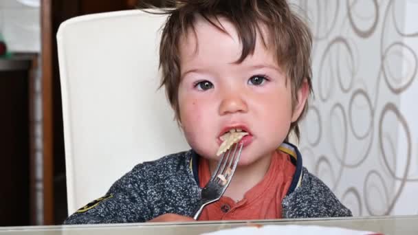 Niño comiendo pasta en la mesa con un tenedor. Almuerzo en un niño de 1-2 años — Vídeo de stock