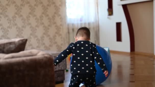 Un niño pequeño está jugando con una pelota. Bebé golpeando su cabeza en una pelota — Vídeo de stock