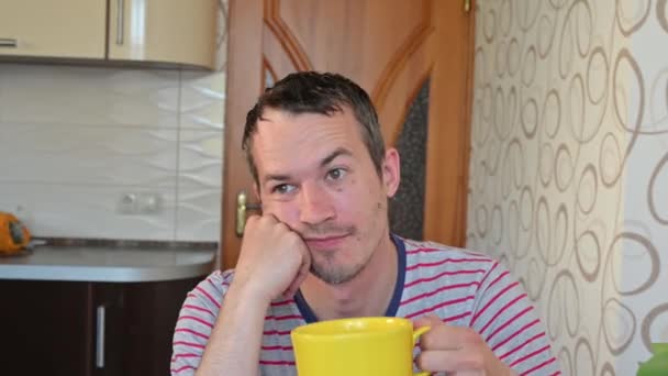 Trauriger junger unrasierter Mann sitzt in der Küche. Quarantäne zu Hause — Stockvideo