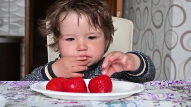 Çocuk beyaz bir tabaktan olgun kırmızı çilekler yiyor. Yakın çekim.