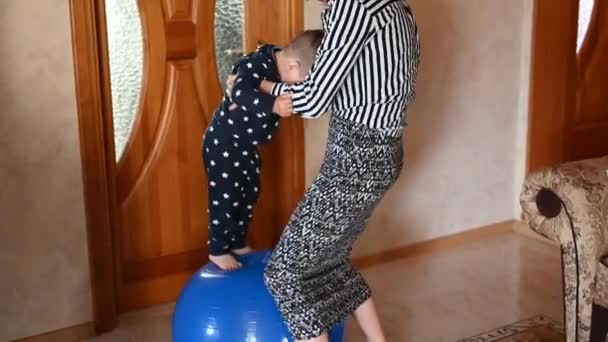 Mamá hace ejercicios corporales en casa con su bebé. Usar una pelota de fitness — Vídeo de stock