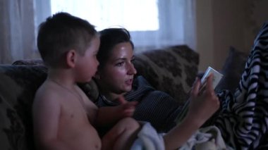 Anne ve çocuk televizyonun önünde kitap okuyorlar.