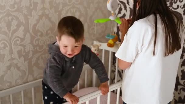 Bebê menino se diverte jogando no berço sob o controle da mãe — Vídeo de Stock