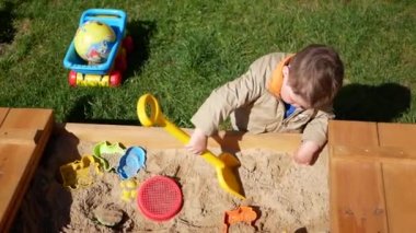 1-2 yaşındaki çocuk kum havuzunda oynuyor. Bir çocuk oyun oynayarak vakit geçirir.