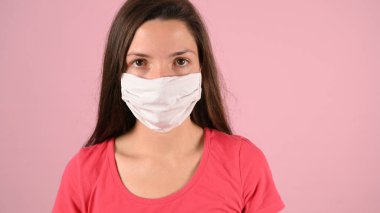 Pembe arka planda koruyucu maskeli bir kız.