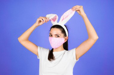 Paskalya Tavşanı 'nın kulaklarında, yüzünde tıbbi koruyucu maske takan genç bir kadın mavi arka planda izole edilmiş. Yüksek kalite fotoğraf