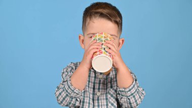 Çocuk mavi arka planda, yakın planda bir bardaktan içer..