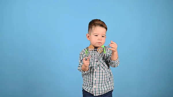 Ребенок держит тележку с едой на синем фоне — стоковое фото