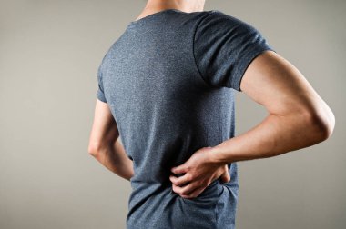 Bir adamın bel ağrısı vardır. Gri arka planda kopyalama alanı olan beyaz bir adam.