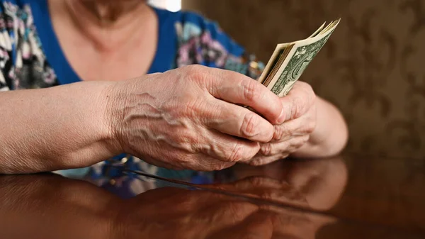 An elderly woman counts dollars. Last money for life, low incomes, poverty, 1 dollar bills