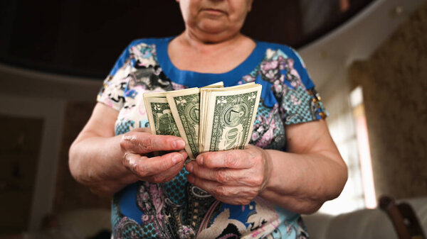 Пожилая женщина считает доллары. Последние деньги на всю жизнь, низкие доходы, бедность, долларовые купюры