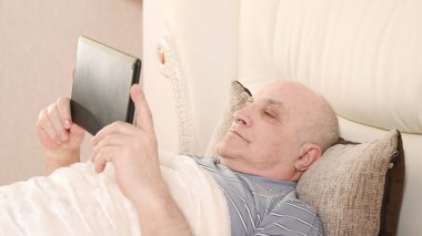 Yatağında tablet olan yaşlı bir adam..