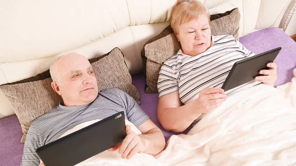 elderly couple with mobile devices in bed, top view.