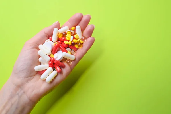 Close up of female hand holding many multi-colored pills on a green background. Health care concept — Stock Photo, Image