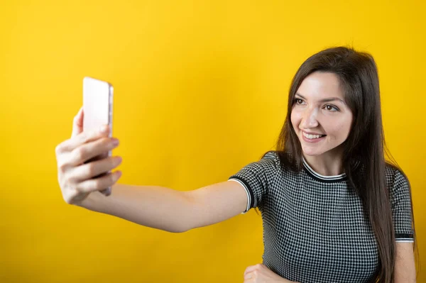 Een jong meisje communiceert via een mobiele telefoon camera, op een gele achtergrond — Stockfoto