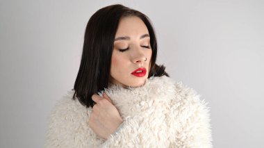 Büyük şekilli kaşları, uzun kirpikleri ve kırmızı dudakları olan genç bir kadın. Beyaz duvarda duran esmer kadın..