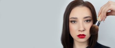 Yüzünde makyaj fırçası olan genç bir kadın. Mükemmel ciltli, kırmızı dudaklı ve burnu delinmiş güzel bir kız.