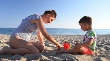 Anne deniz kenarında tatilde çocukla oynuyor..