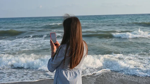 在电话里给大海拍照的年轻女人 — 图库照片