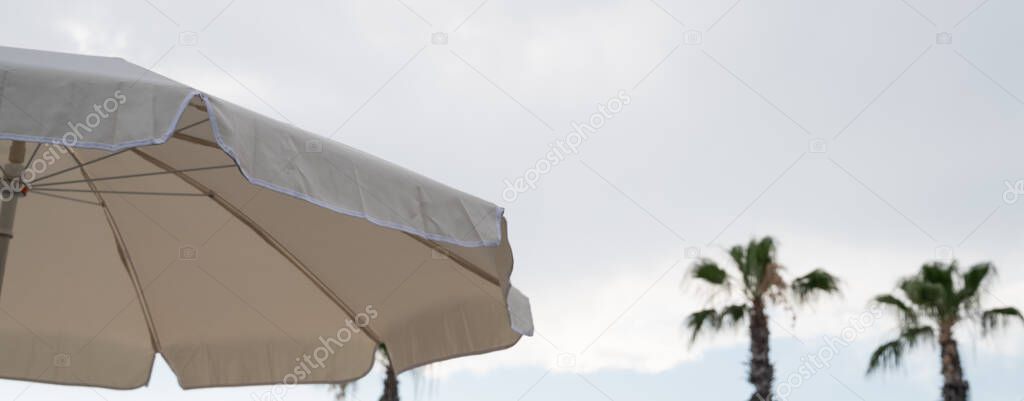White sunshade and parasol on clear beach sand. Striped wooden wall painted in white color with blue sky and white clouds. Simplicity of white beach landscape with nobody. . High quality photo