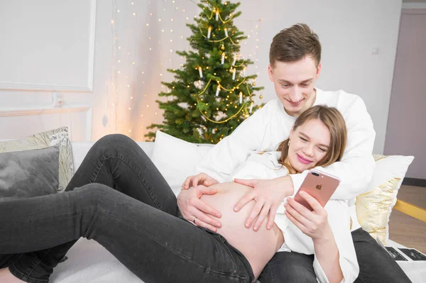 Gülümseyen çift evde birlikte rahatlıyor online alışveriş yapıyorlar akıllı telefondan sipariş alıyorlar. Noel arkaplanı.