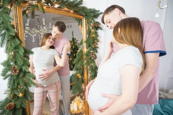Aynadaki genç hamile çift. Noel süsleri. Hamilelik, kış tatili ve insanların konsepti.